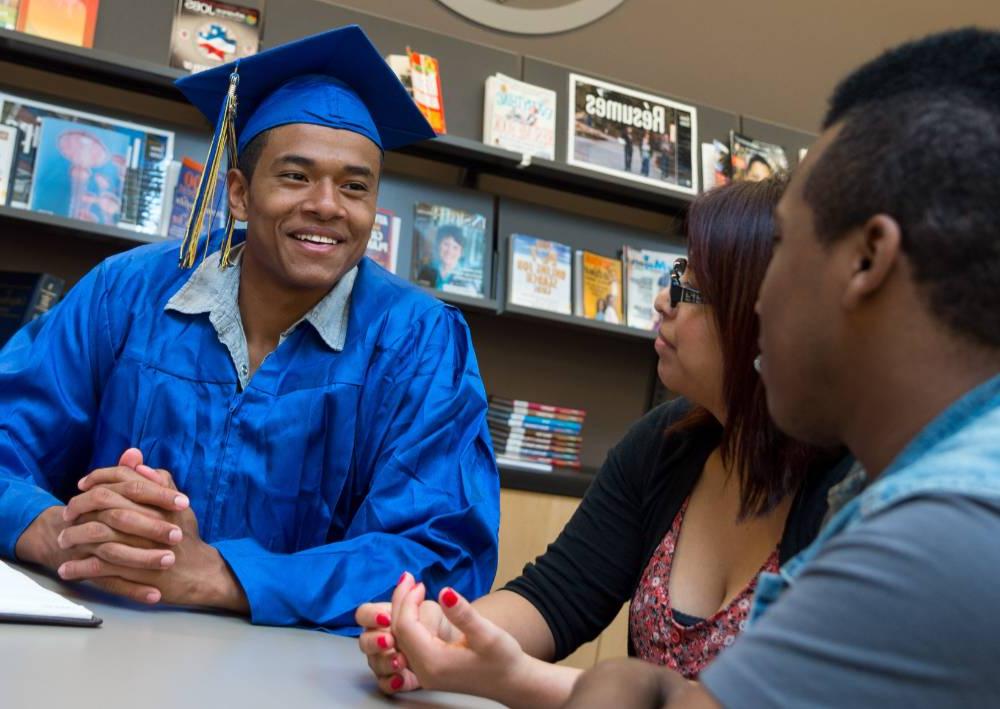 A student in graduation regalia sits at the career center with a career counselor